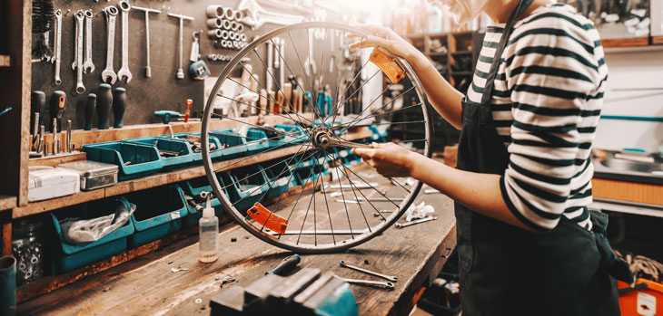 Woman holding a bicycle tire in a workshop. PHoto by iStock.