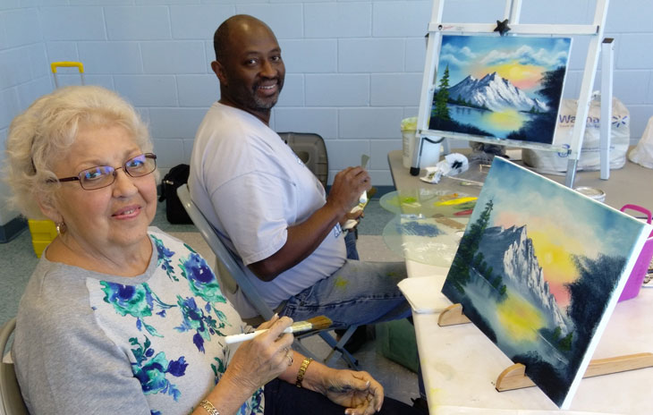 A man and a woman with paintings they are working on at an art class inside Wickham Park Community Center.