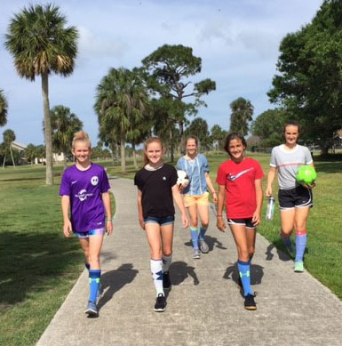 Five teen-age girls walking on sidewalk at golf course to play footgolf