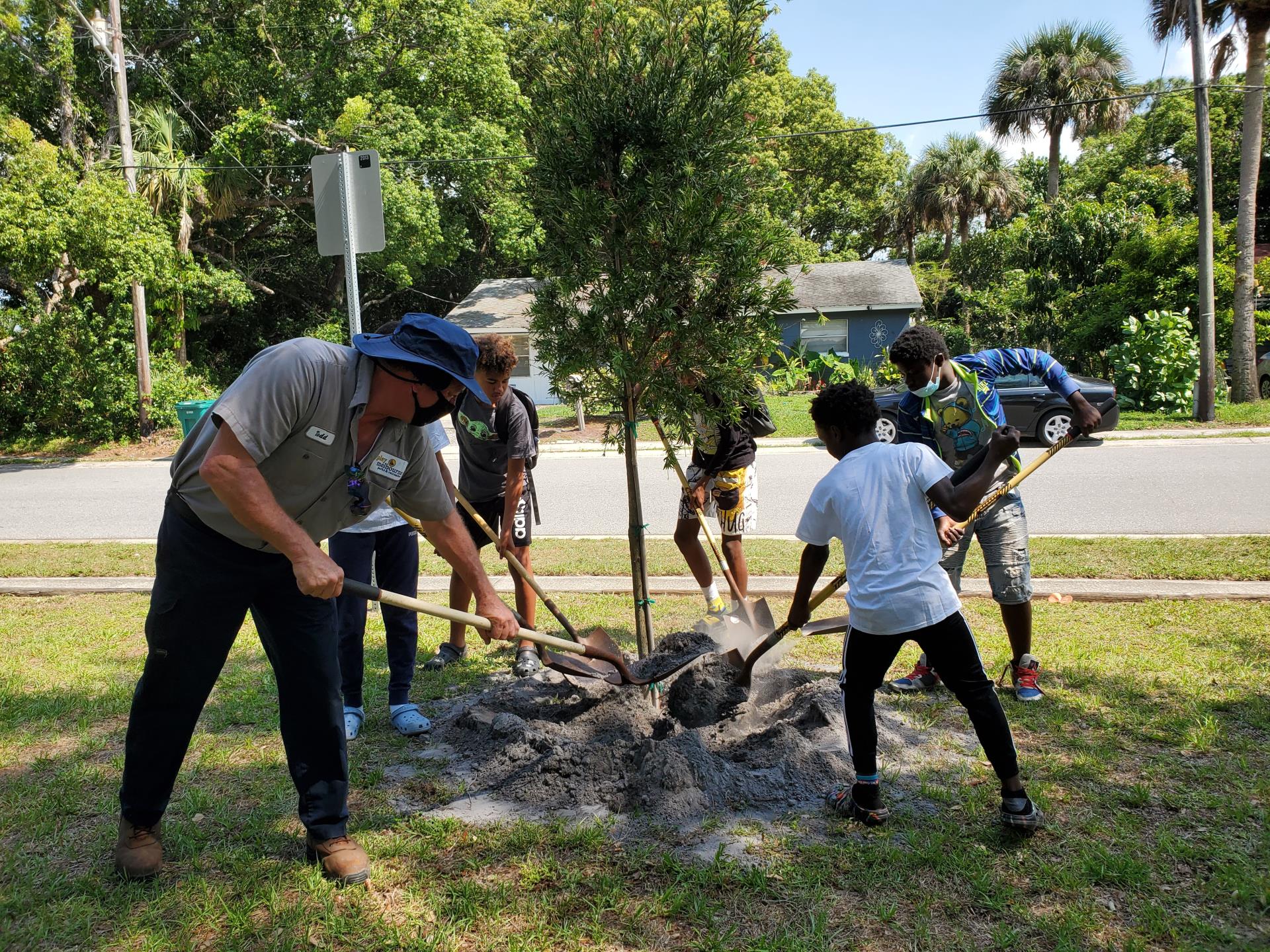 A city employee and a group of children help plant a tree.