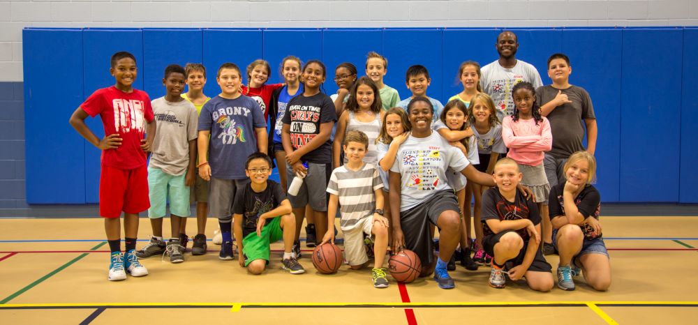 Group picture of kids and two camp counselors inside a gym.