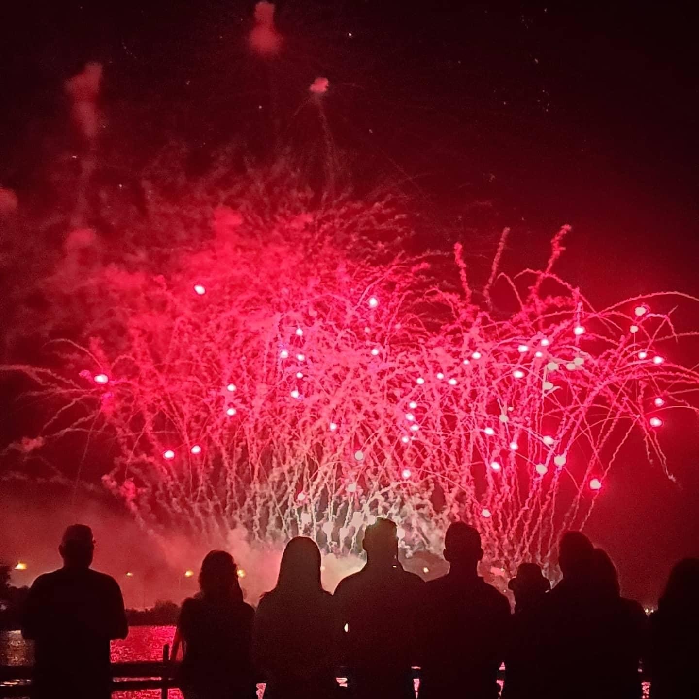 Red fireworks in the night sky with the silhouettes of spectators in the foreground.