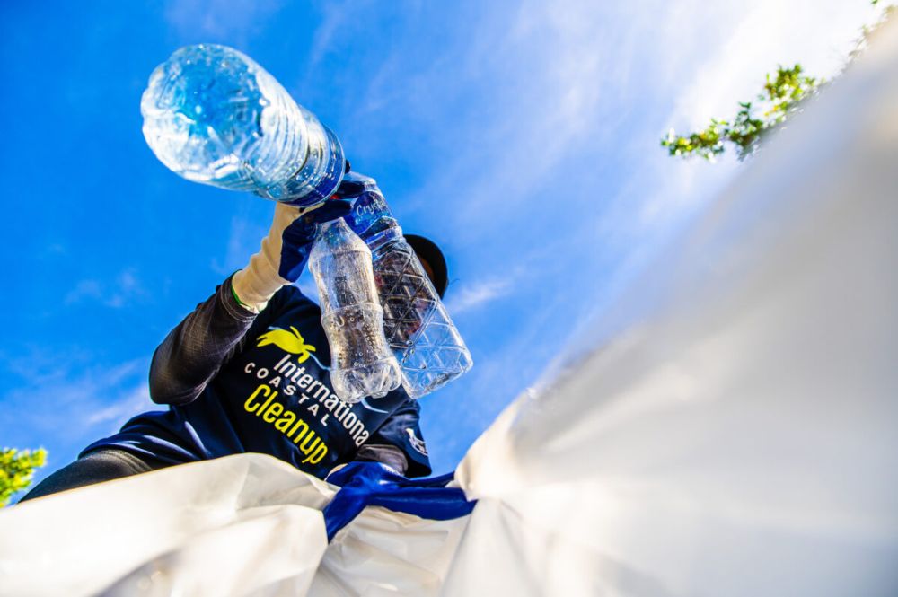 Man wearing an International Coastal Cleanup shirt puts plastic bottles into a bag. Source: Ocean Conservancy, credit Keegan Callender