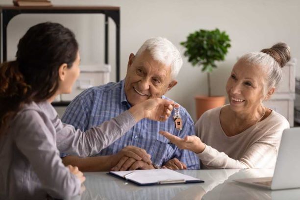 Woman gives keys to an elderly woman who is smiling and sitting next to her husband.