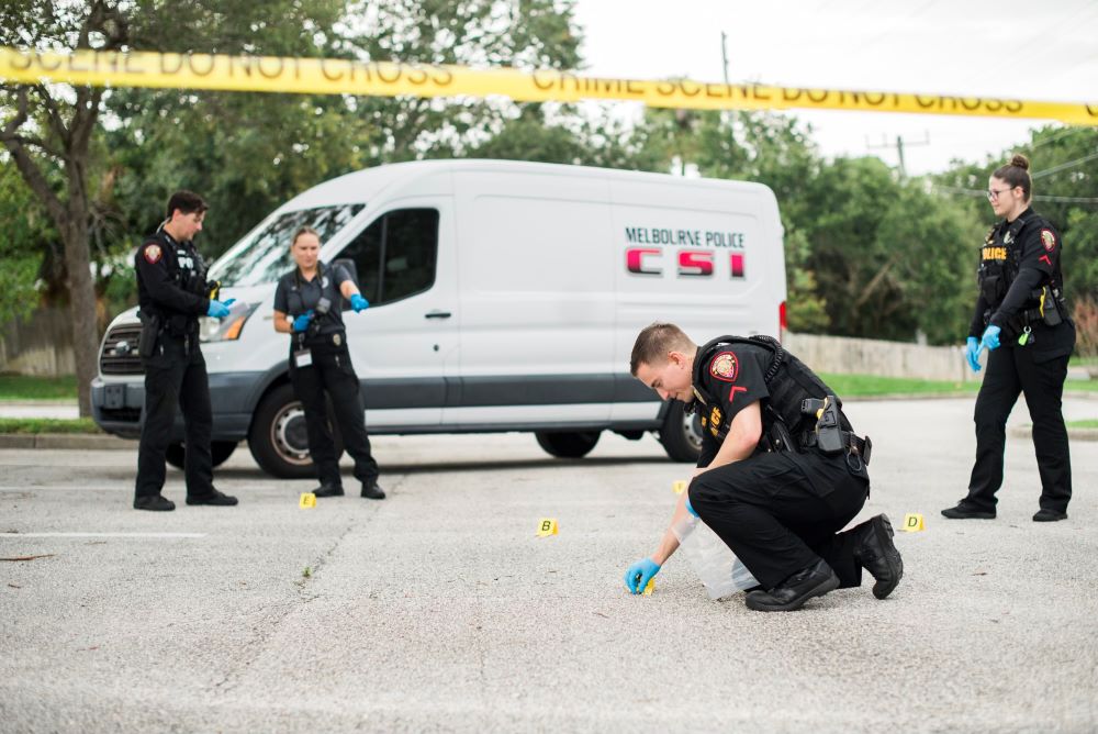 Police officers collecting items in front of a Melbourne CSI van with yellow crime scene tape in the foreground.