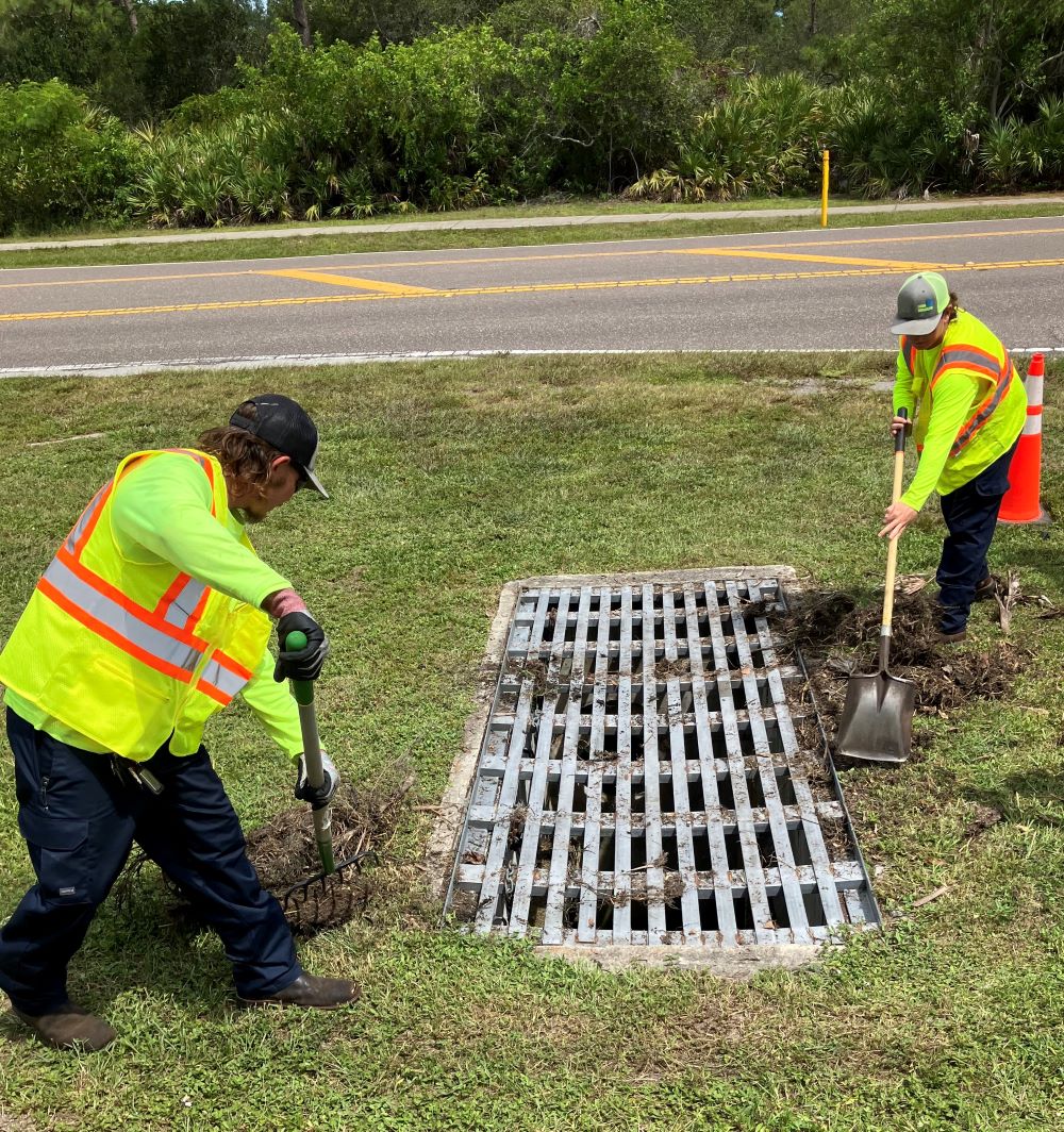 Two employees clear debris from a storm drain.