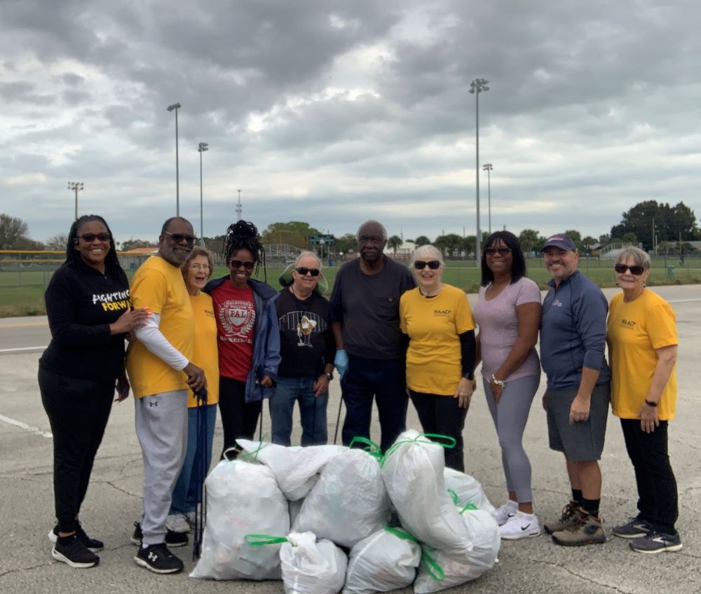 Group of 8 Adopt-a-Road volunteers smiling and standing next to a pile of filled trash bags.