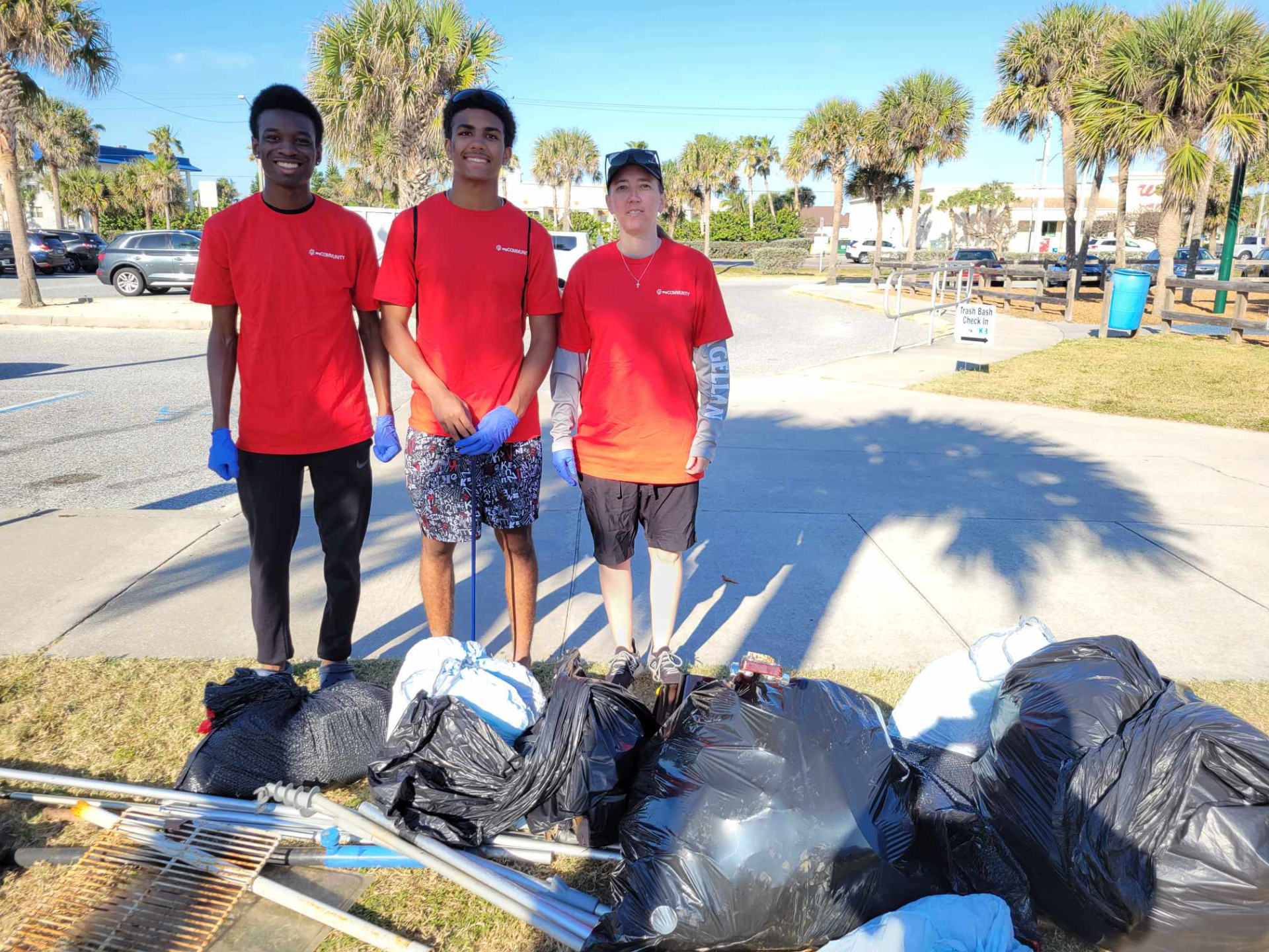 Group of three Trash Bash volunteers standing in front of a pile of filled trash bags and other items collected during the clean-up event.