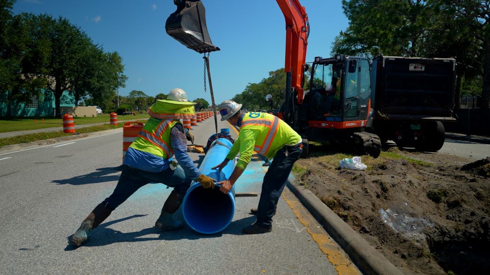 Workers moving a water main pipe into place.