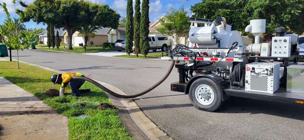 Employee puts hose from truck into small hole near a water meter in the right of way