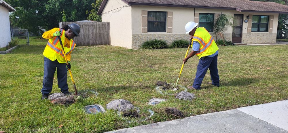 Two city employees each digging one small hole next to a water meter