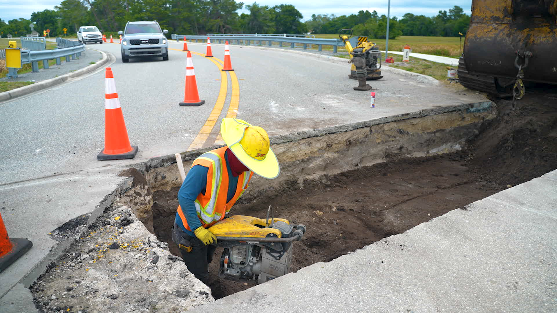 Worker packing down soil in a small section of road that has been cut away.