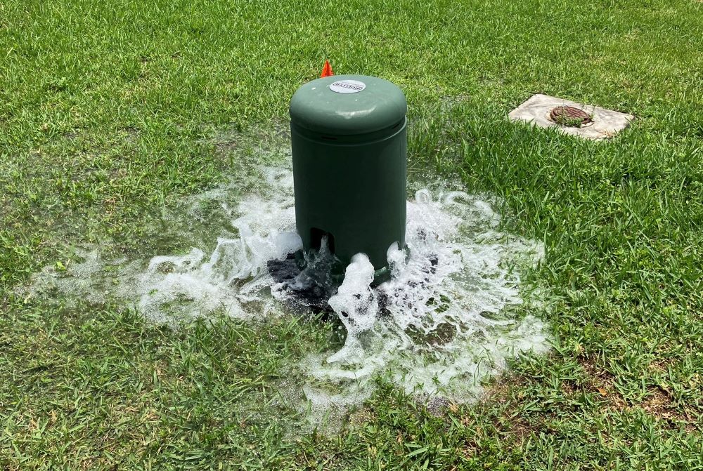 Water flowing from the bottom of an Automatic Flushing Valve onto the grass.