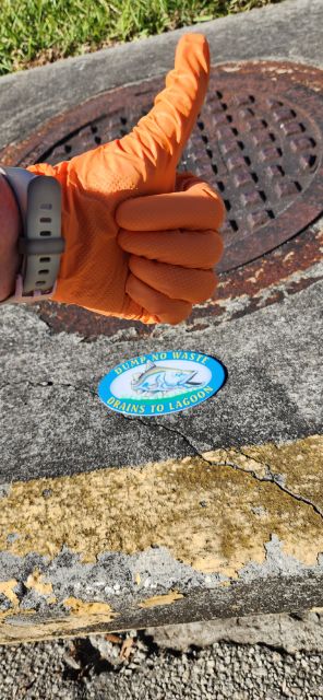 A hand giving the "thumbs up" sign in front of a storm drain with a marker