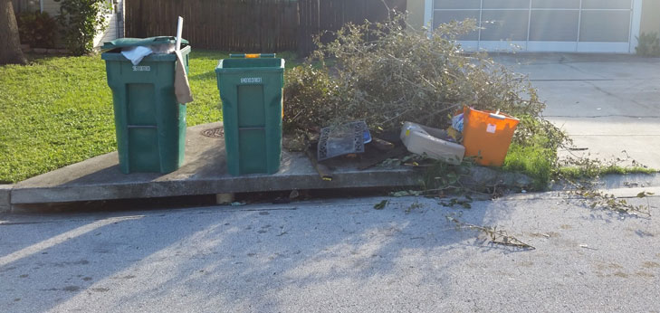 Trash cans, yard debris and other trash stacked on top of a stormwater inlet