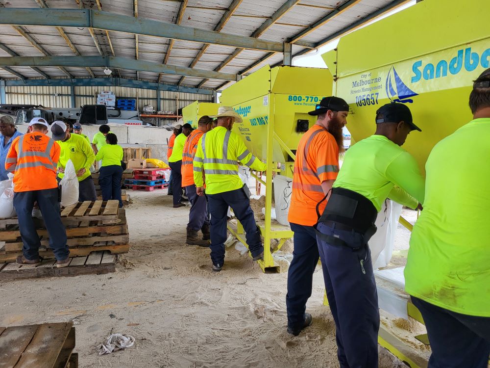 Employees filling sandbags using sandbagger machine